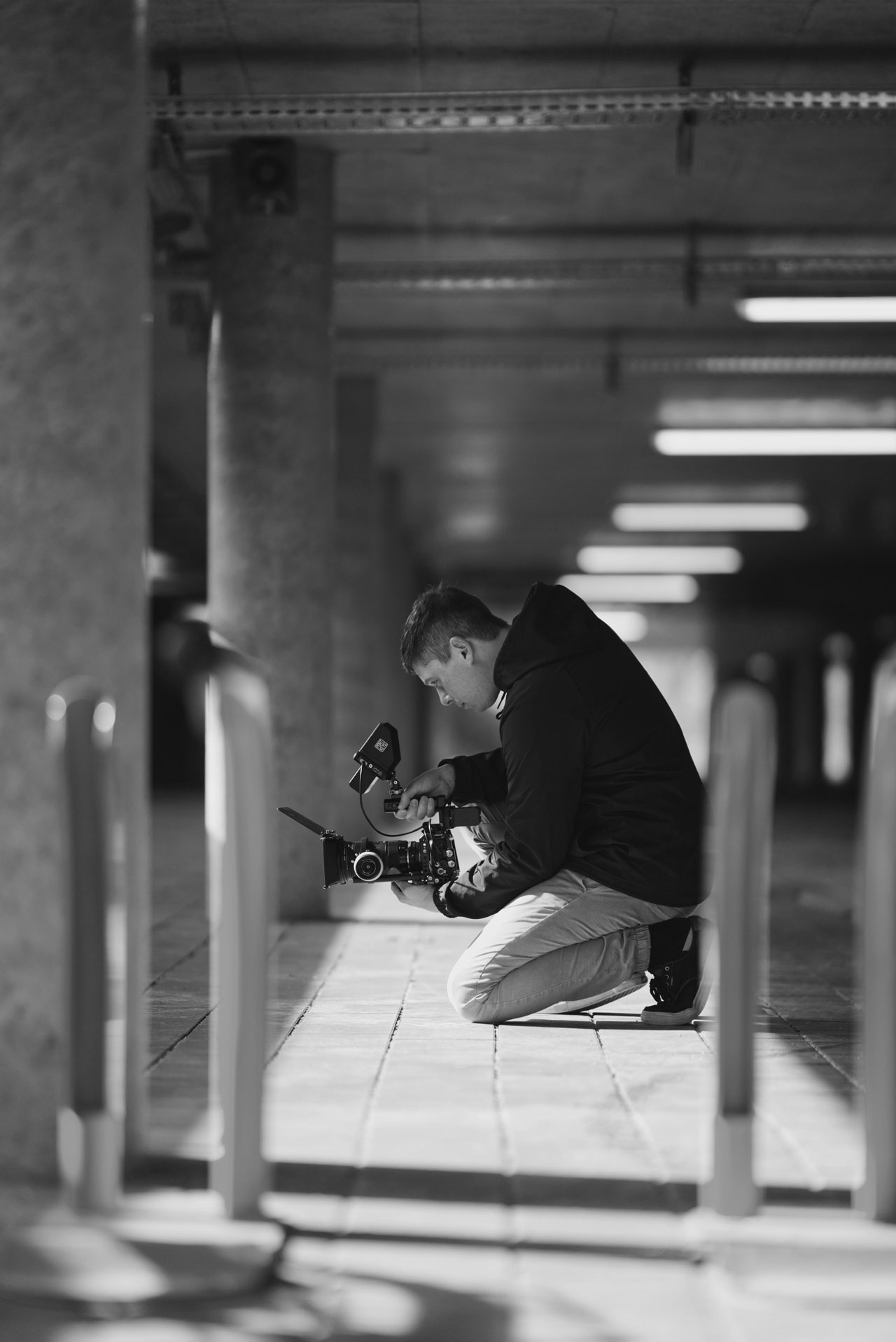 Ein Mann kniet im Parkhaus und hält eine Kamera, während er auf den Boden fokussiert.