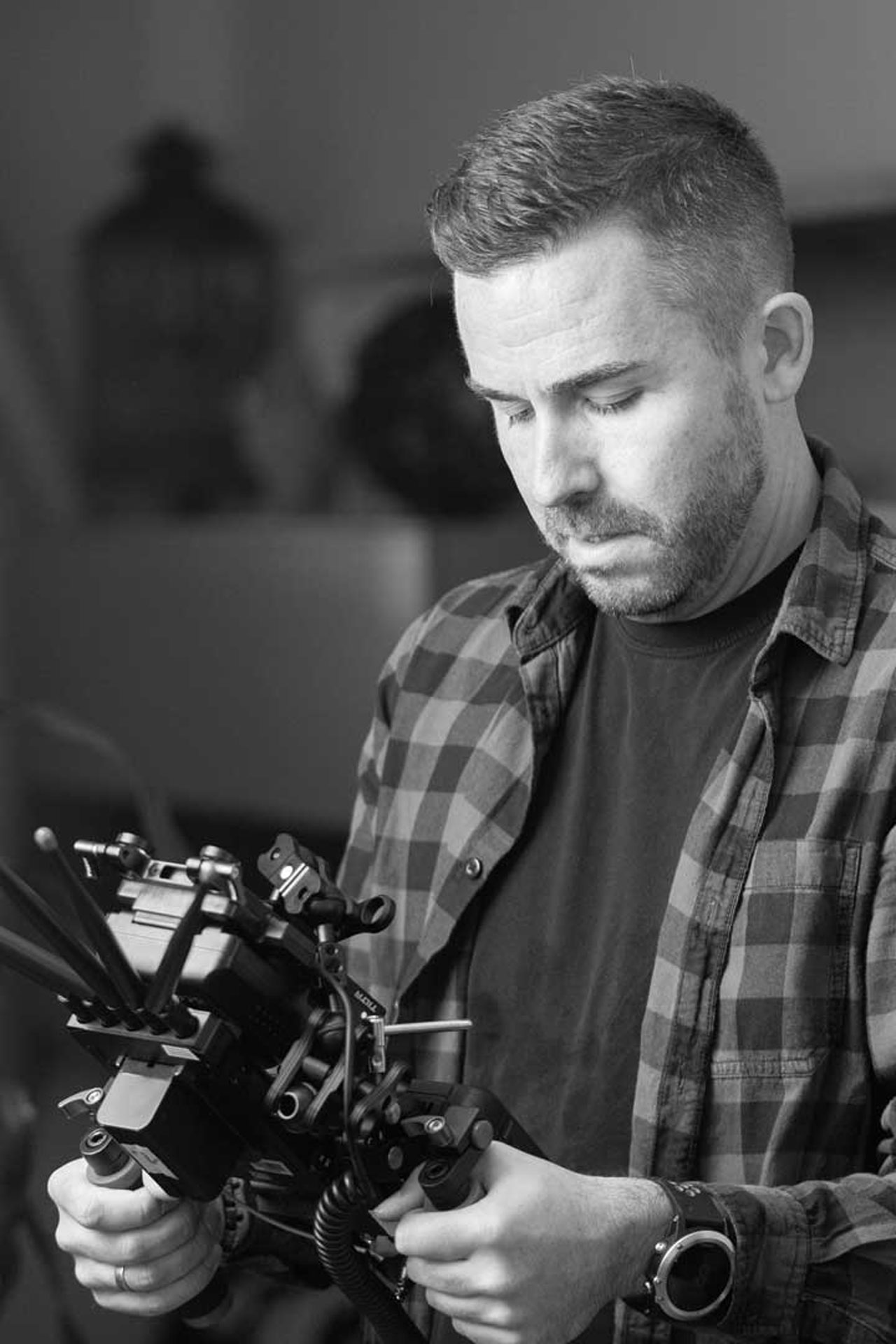 Mann in einem karierten Hemd, der eine Kameraausrüstung in den Händen hält, in Schwarz-Weiß.