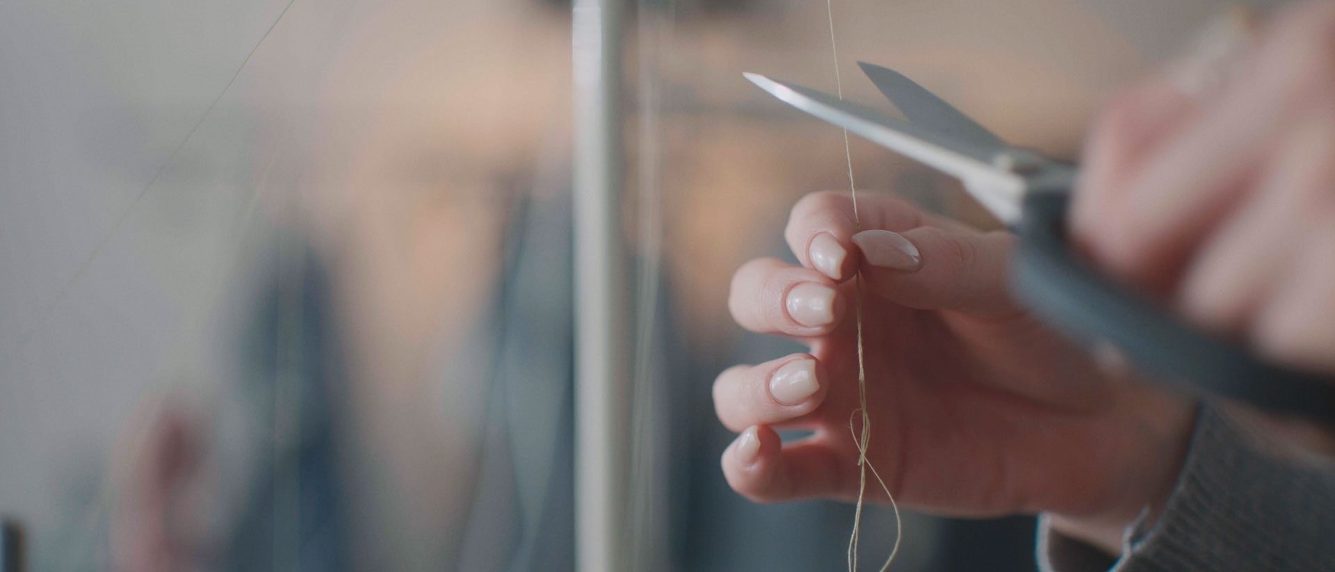Eine Hand schneidet mit einer Schere einen Faden ab, während eine andere Hand den Faden hält.