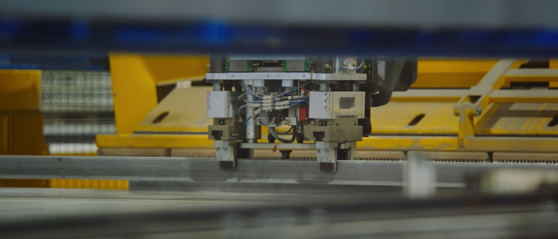 Industrieroboter mit Greifarmen, der eine Metallstange in einer Umlaufanlage bearbeitet.