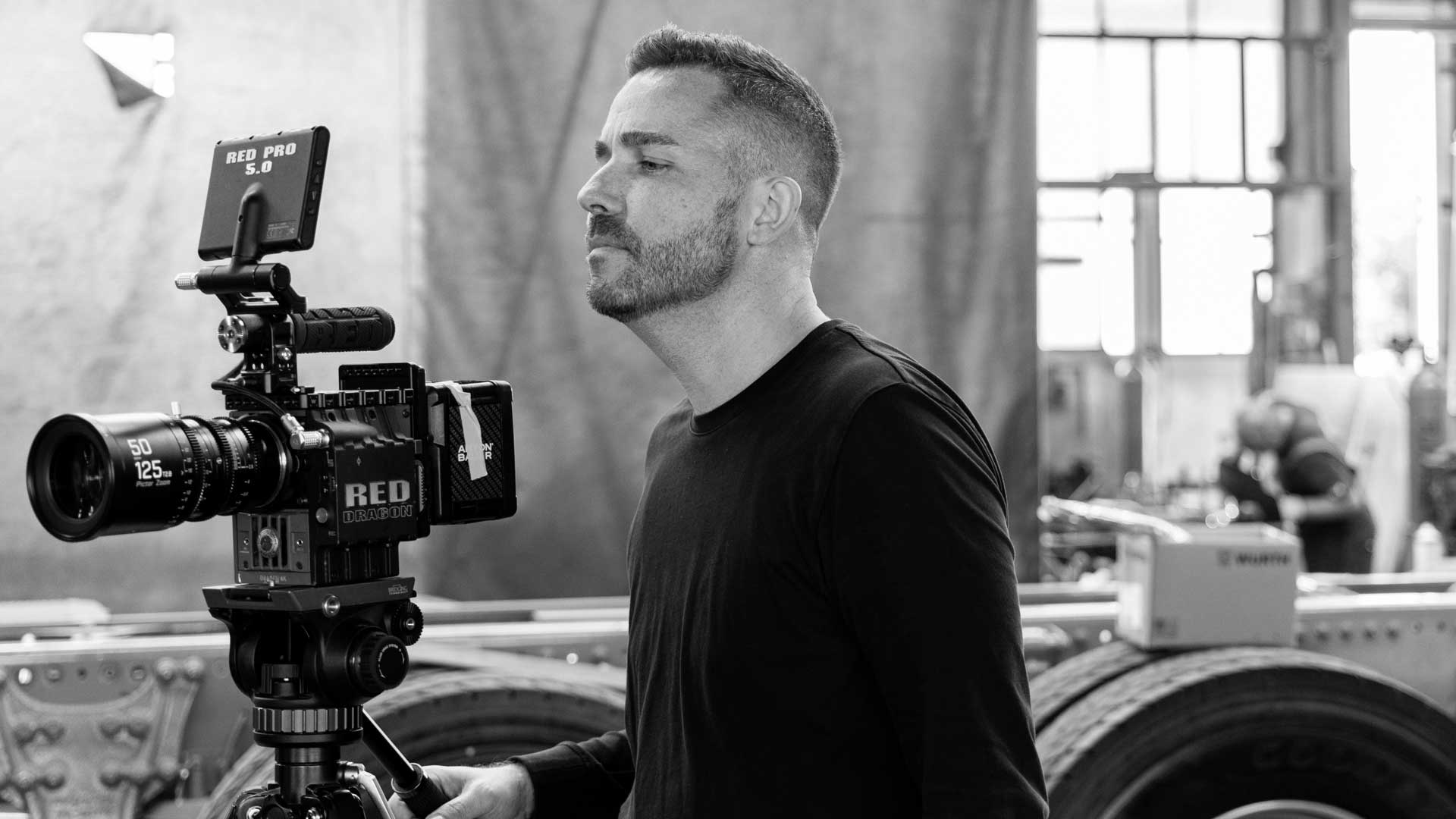 Mann steht neben einer RED Kamera und fokussiert auf das Objektiv während der Aufnahme.