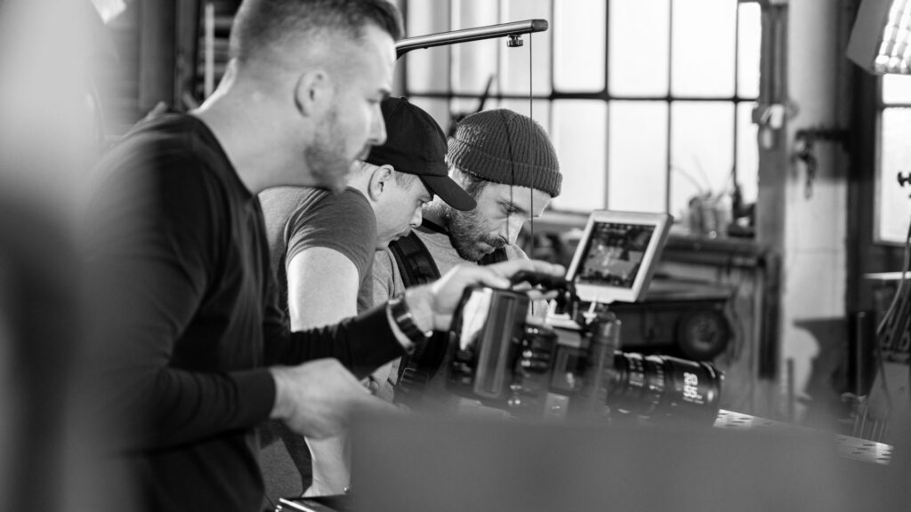 Drei Männer, die an einer Kameraausrüstung in einem Innenraum arbeiten.