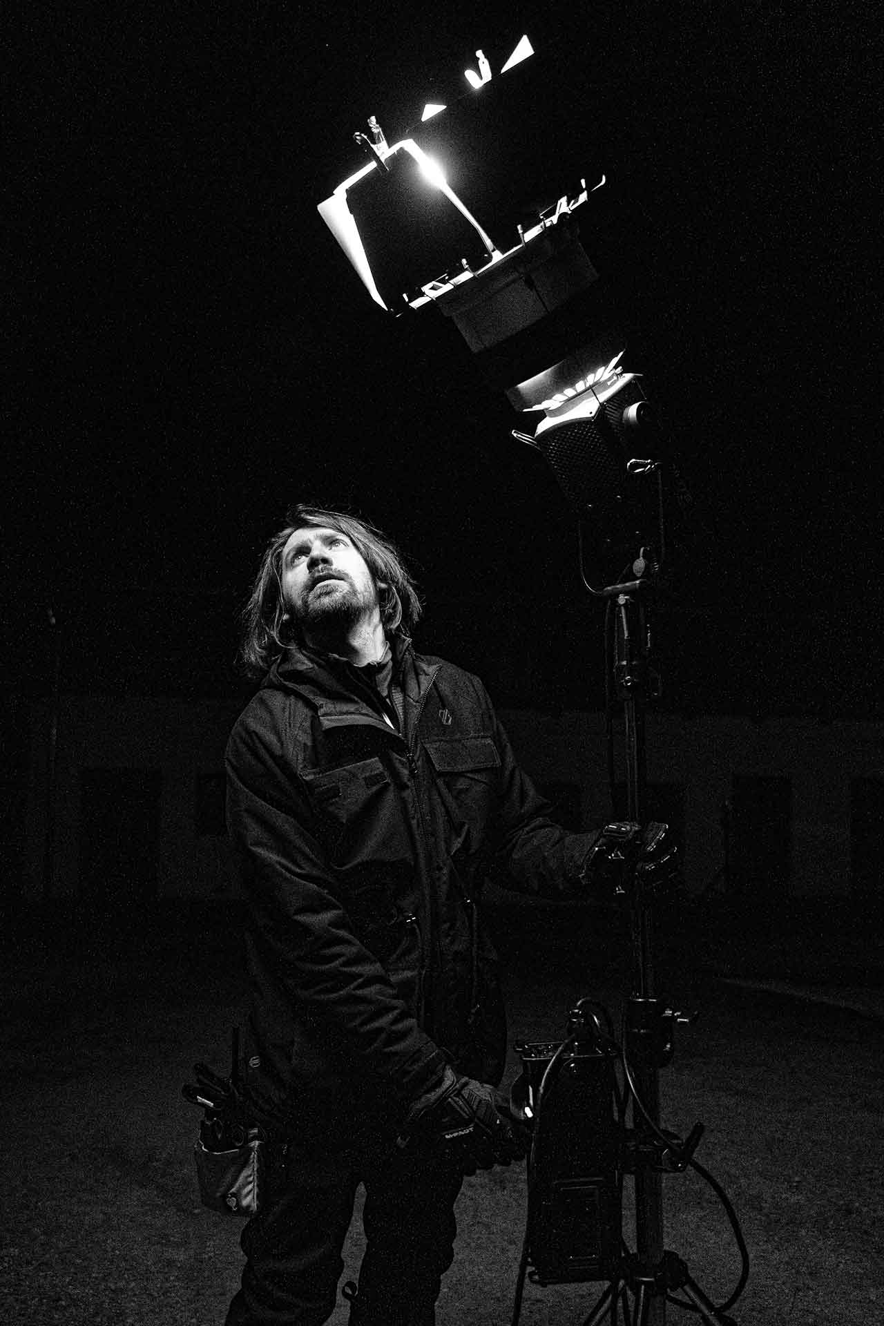 Ein Mann steht unter einem Scheinwerfer und schaut nach oben, während er eine Kameraausrüstung hält.